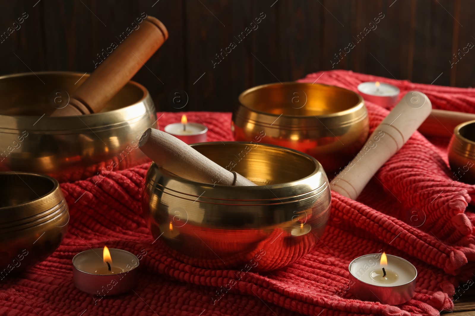 Photo of Tibetan singing bowls with mallets and burning candles on red fabric