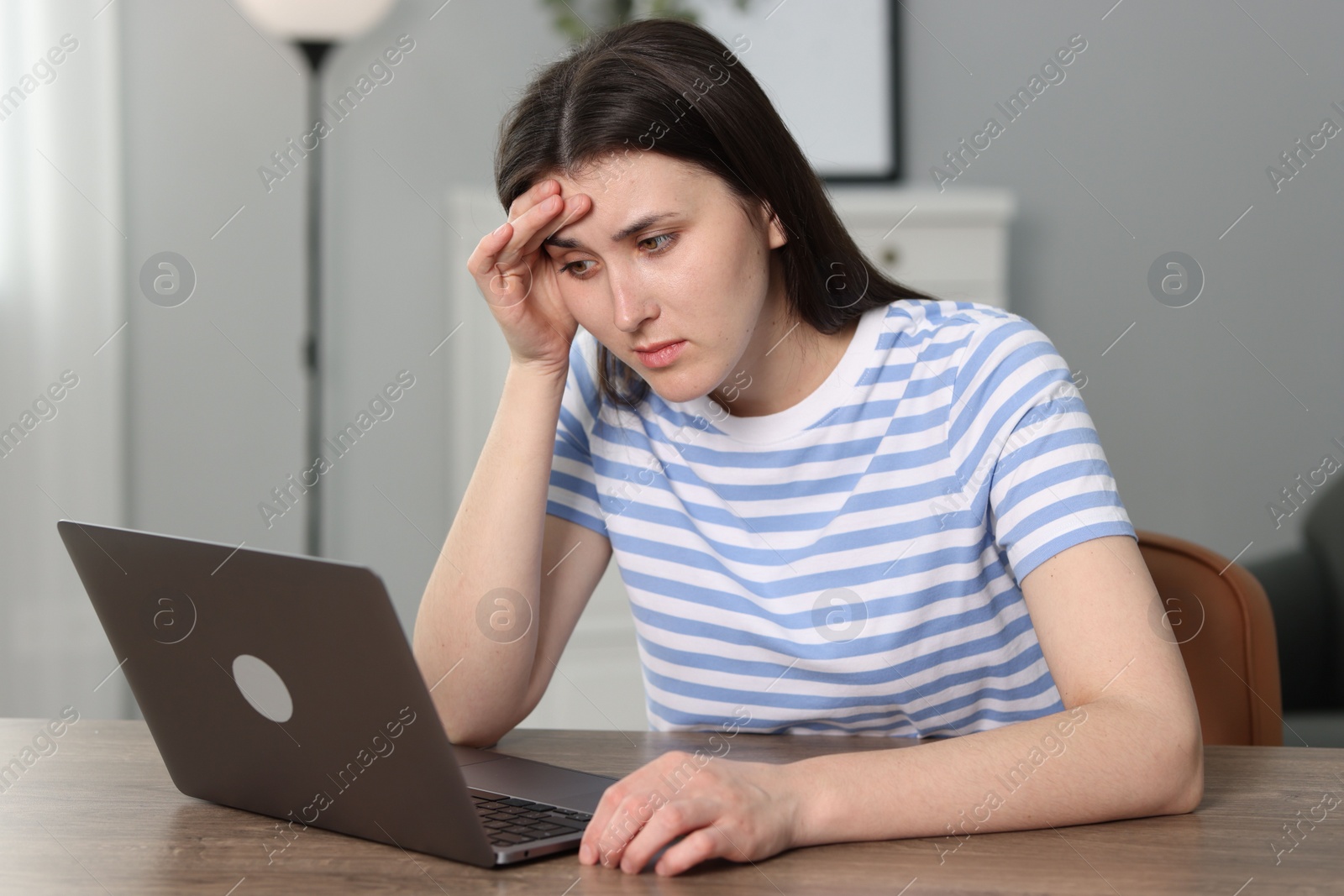 Photo of Overwhelmed woman sitting with laptop at table indoors
