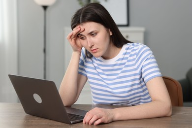 Overwhelmed woman sitting with laptop at table indoors