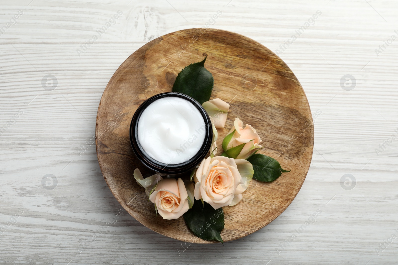 Photo of Plate with jar of organic cream and rose flowers on white wooden table