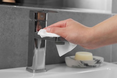 Photo of Woman cleaning faucet of bathroom sink with paper towel, closeup