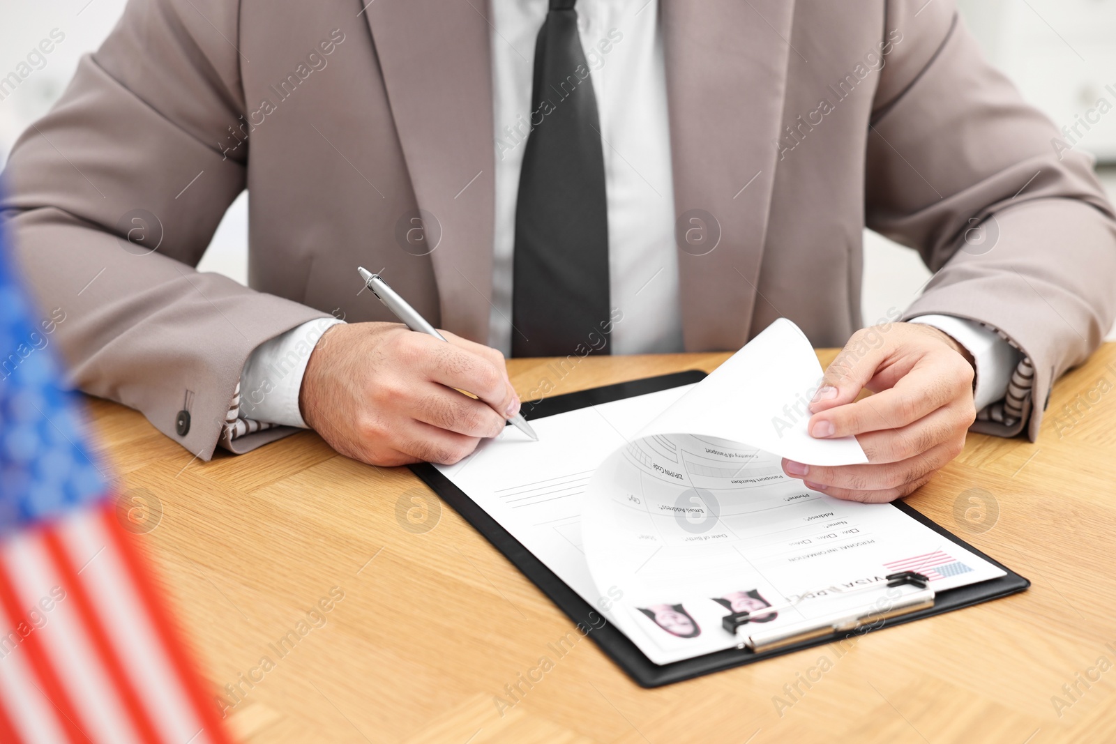 Photo of Immigration to United States of America. Embassy worker signing visa application form at wooden table, closeup