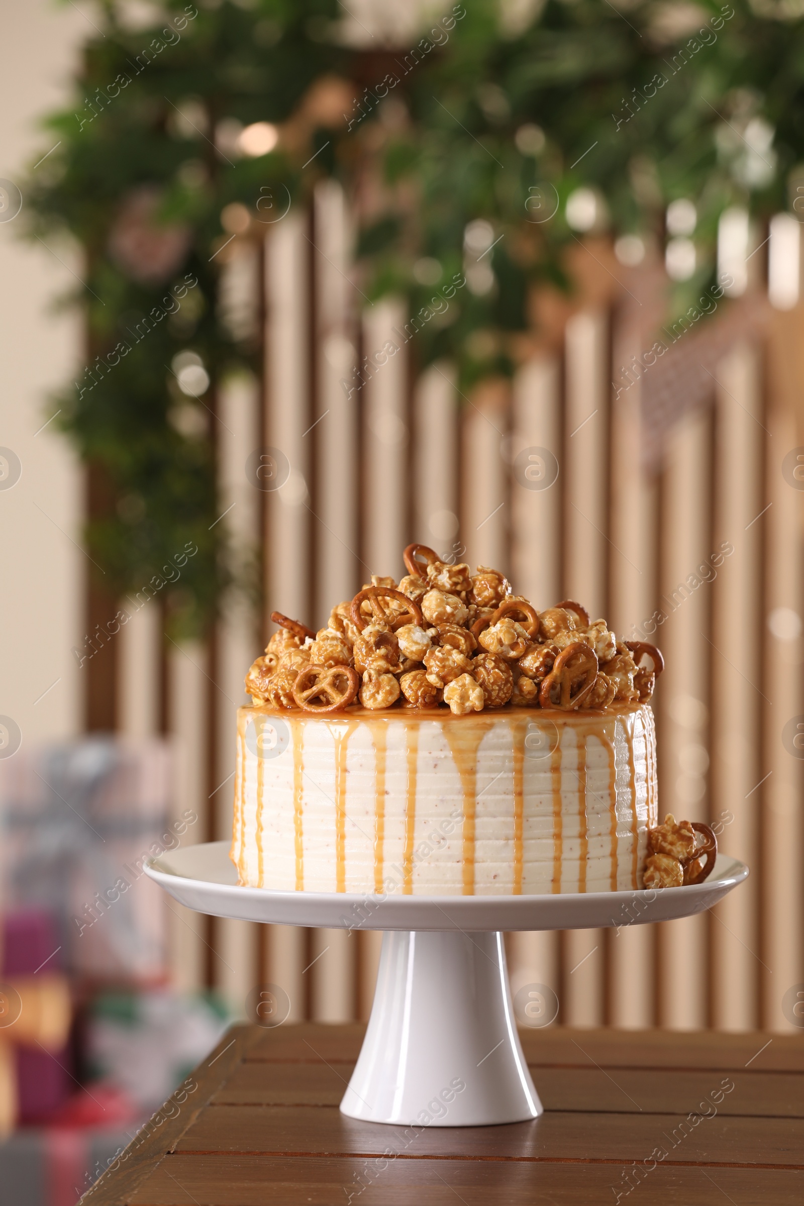 Photo of Caramel drip cake decorated with popcorn and pretzels on wooden table, space for text