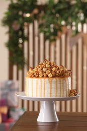 Photo of Caramel drip cake decorated with popcorn and pretzels on wooden table, space for text