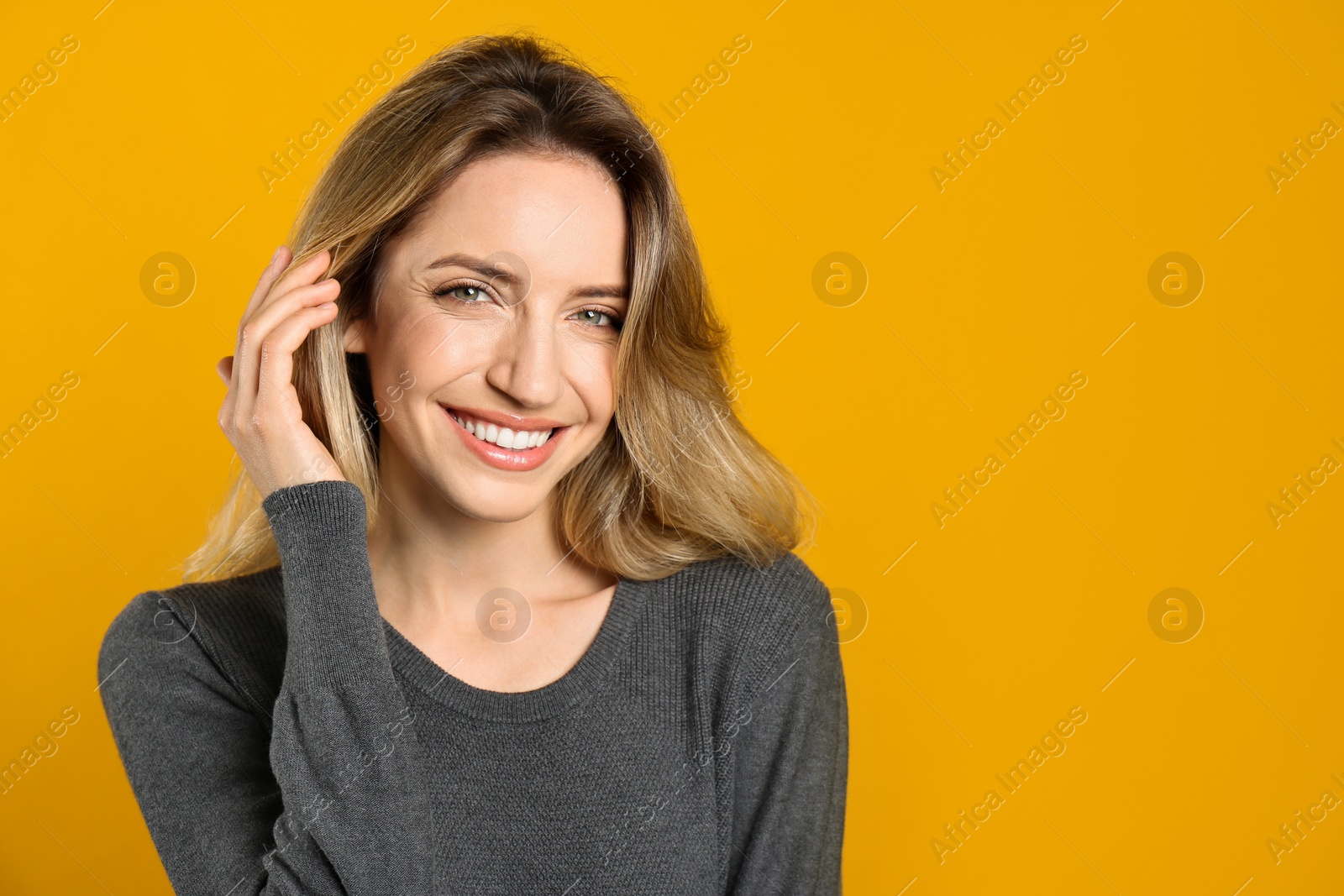 Photo of Portrait of happy young woman with beautiful blonde hair and charming smile on yellow background. Space for text