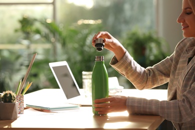 Woman with green thermos bottle at workplace