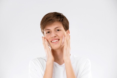 Teenage boy with problem skin applying anti acne cream on light background