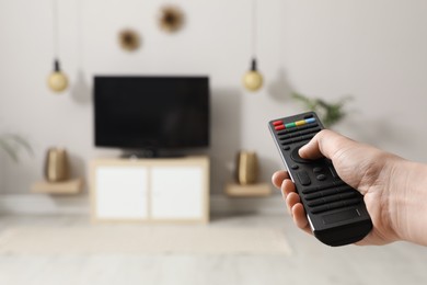 Photo of Young man switching channels on TV set with remote control at home, closeup