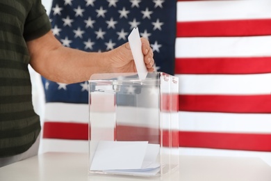 Elderly woman putting ballot paper into box and American flag on background, closeup