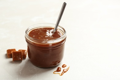 Photo of Jar with tasty caramel sauce and spoon on light background. Space for text