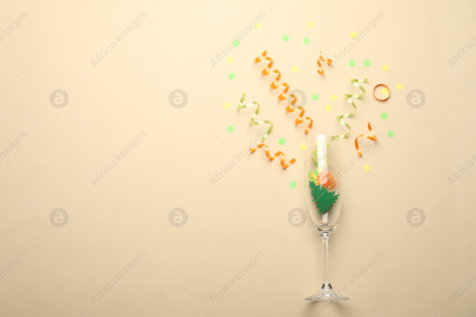 Photo of Glass and shiny confetti on beige background, flat lay. Space for text