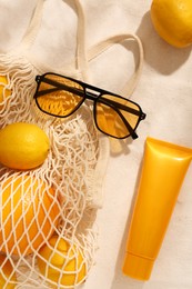 Photo of String bag with sunglasses, fruits and sunscreen on sand, flat lay