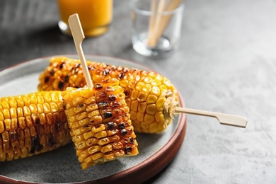 Plate with delicious grilled corn cobs on gray table, closeup