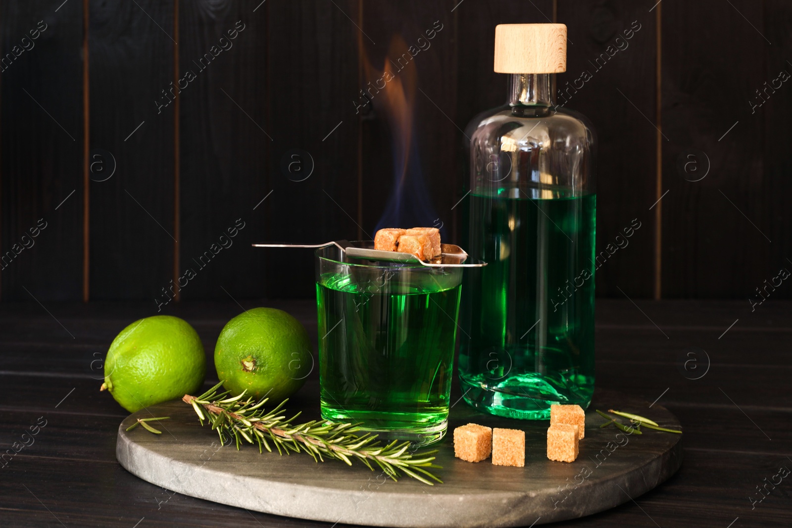 Photo of Absinthe in glass, flaming brown sugar, rosemary and lime on wooden table. Alcoholic drink