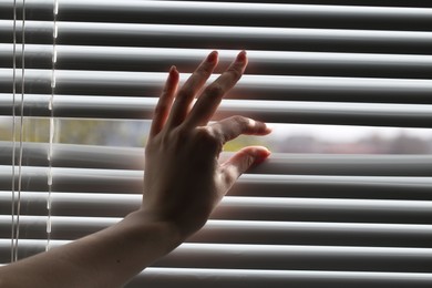 Woman separating slats of white blinds indoors, closeup