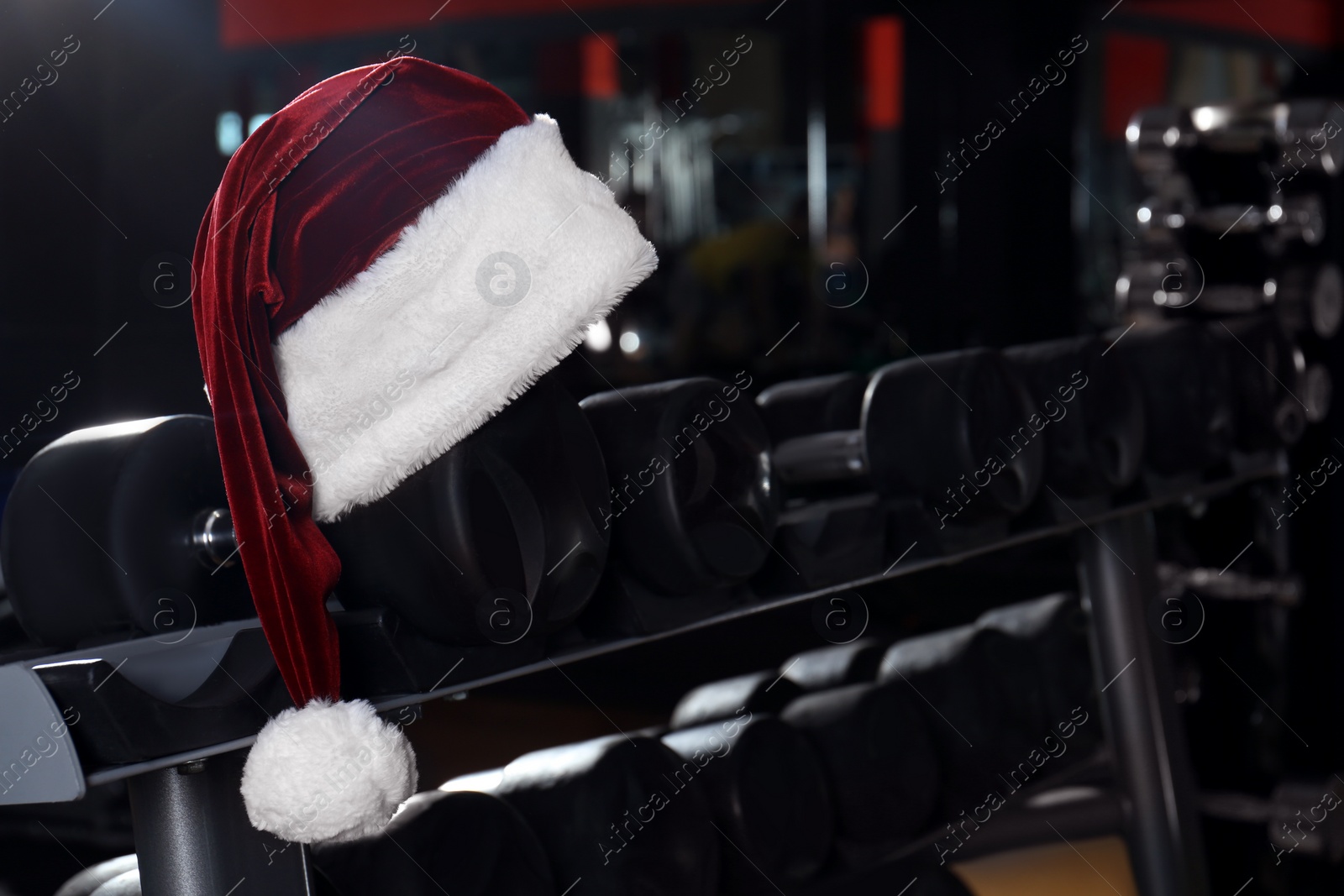 Photo of Santa hat on stand with dumbbells in modern gym