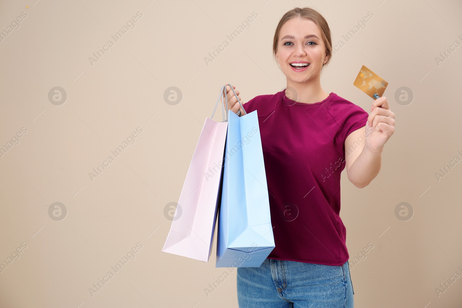 Photo of Portrait of happy young woman with credit card and shopping bags on color background, space for text. Spending money