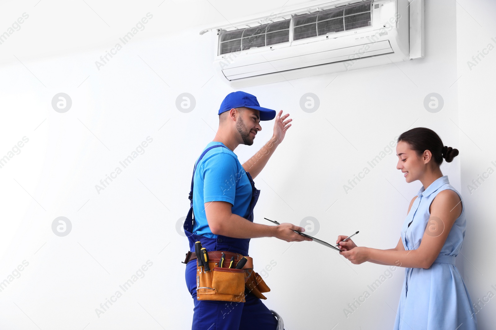 Photo of Professional technician speaking with woman about air conditioner indoors