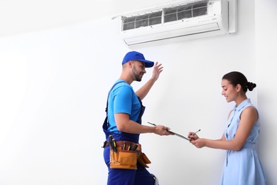 Professional technician speaking with woman about air conditioner indoors