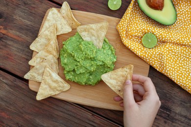 Photo of Woman holding nachos and delicious guacamole made of avocados at wooden table, closeup
