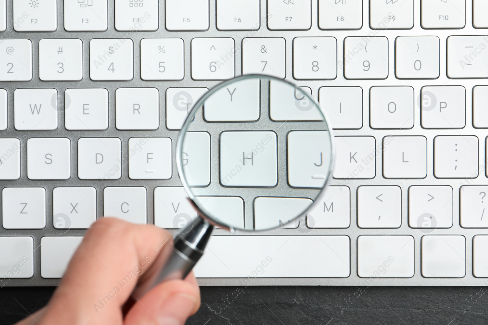 Photo of Woman holding magnifier glass over keyboard on black slate table, top view. Find keywords concept