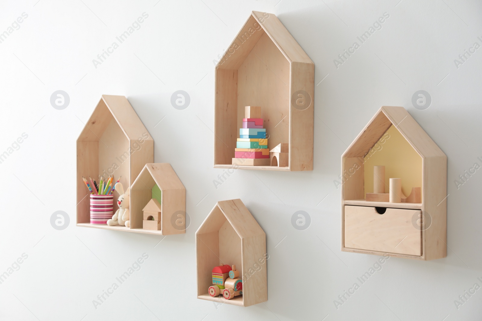 Photo of Different house shaped shelves with toys on white wall. Interior design