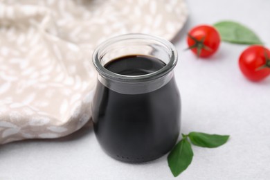 Photo of Glass jar with balsamic vinegar, basil and tomatoes on white table