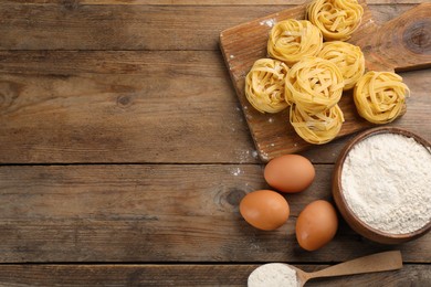 Uncooked homemade pasta and ingredients on wooden table, flat lay. Space for text