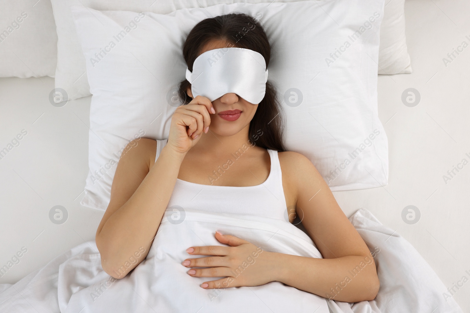 Photo of Unhappy young woman with sleeping mask in bed, top view