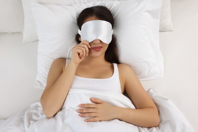 Unhappy young woman with sleeping mask in bed, top view