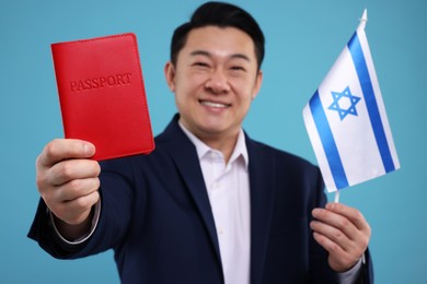 Photo of Immigration. Happy man with passport and flag of Israel on light blue background, selective focus