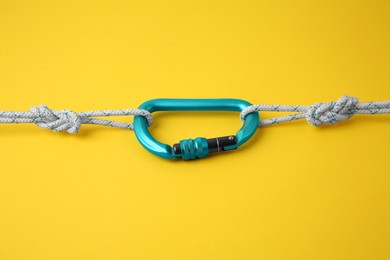 Photo of One metal carabiner with ropes on yellow background