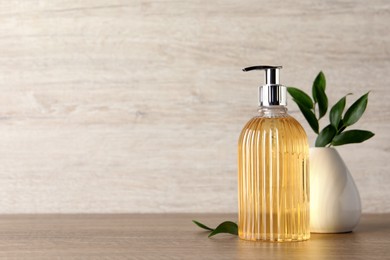 Photo of Stylish dispenser with liquid soap and green leaves in vase on wooden table, space for text