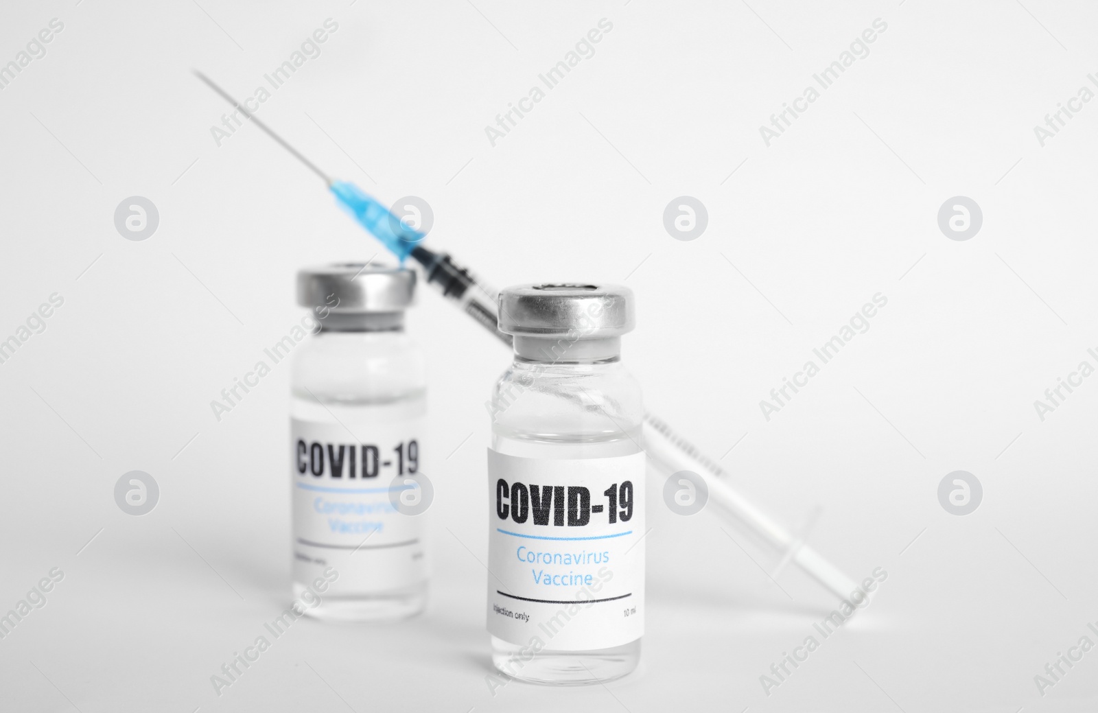 Photo of Vials with coronavirus vaccine and syringe on white background