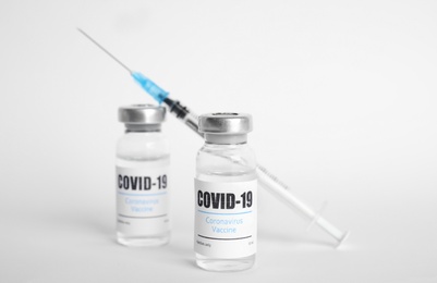 Photo of Vials with coronavirus vaccine and syringe on white background