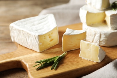 Wooden board with delicious cheeses on table, closeup