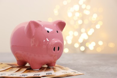 Photo of Piggy bank with euro banknotes on grey table against blurred lights, space for text