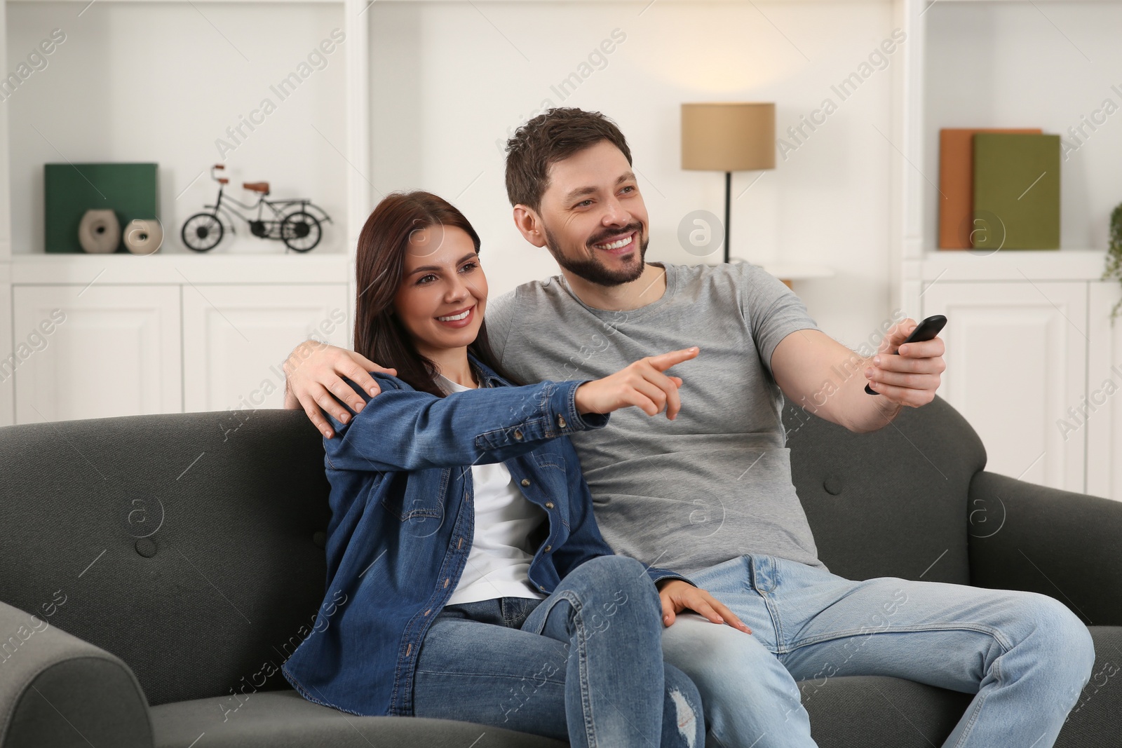 Photo of Happy couple watching show at home. Man changing TV channels with remote control