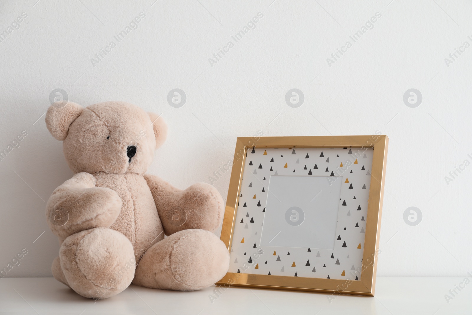 Photo of Empty photo frame and teddy bear on table near white wall. Space for design