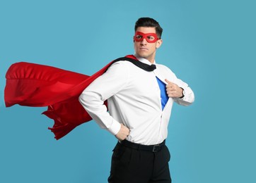 Photo of Businessman in superhero cape and mask taking shirt off on light blue background