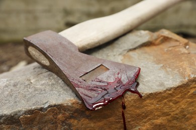 Axe with blood on stone outdoors, closeup