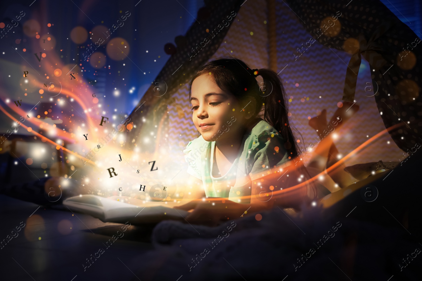 Image of Girl reading shiny magic book with letters flying over it in play tent at home