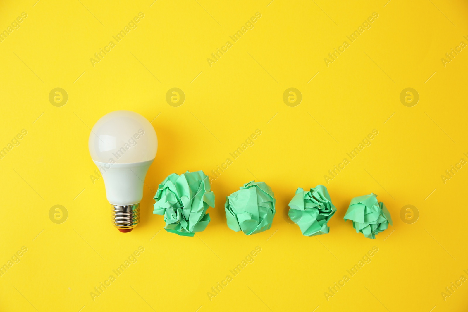 Photo of Flat lay composition with lamp bulb and crumpled paper on color background