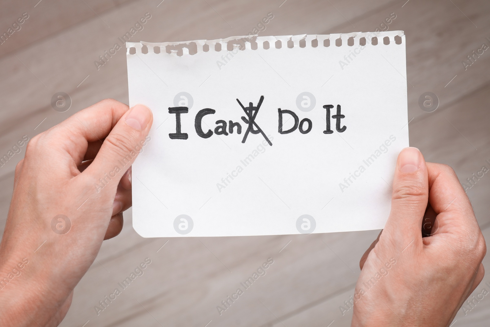 Photo of Motivation concept. Woman holding paper with changed phrase from I Can't Do It into I Can Do It by crossing over letter T indoors, closeup