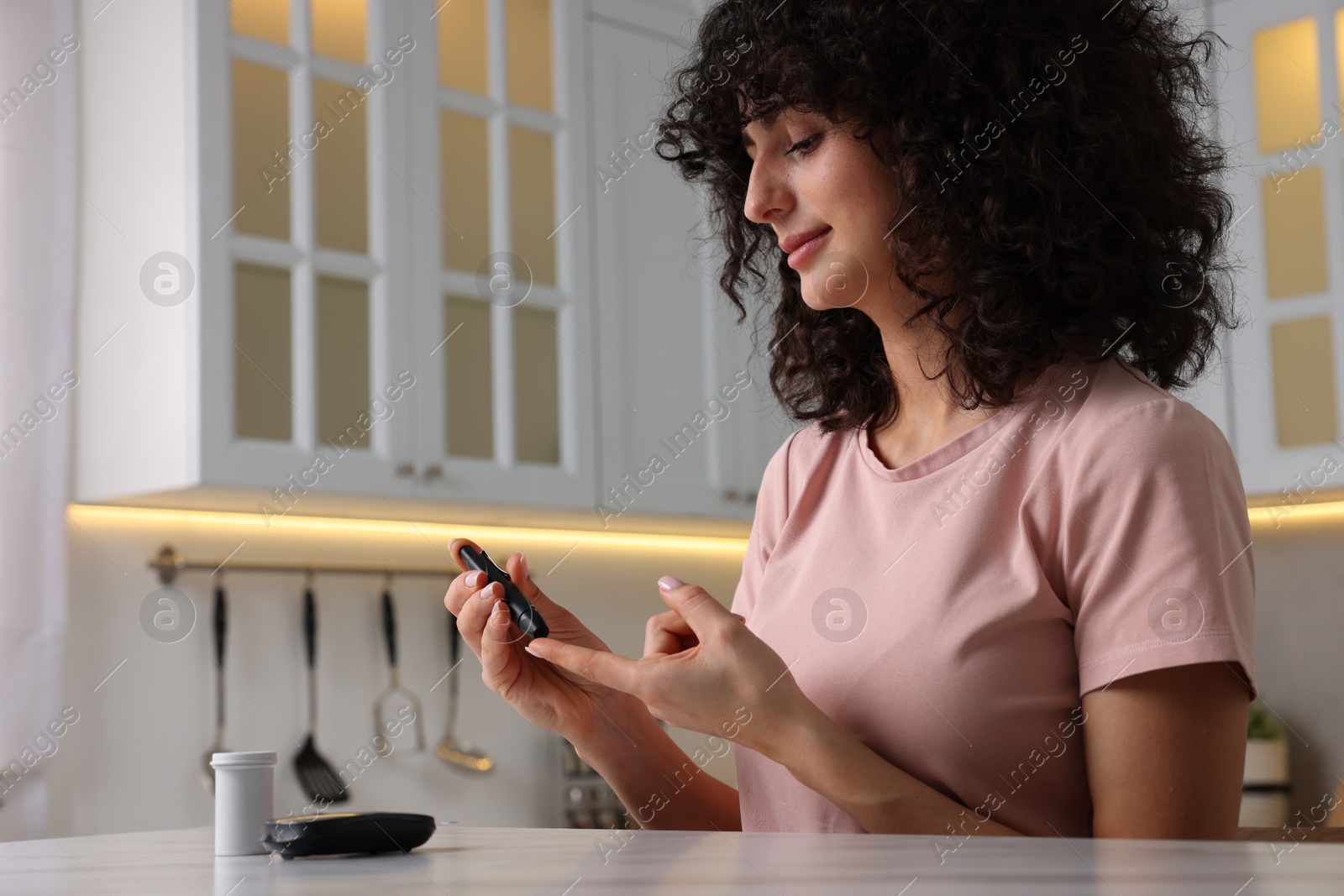 Photo of Diabetes. Woman using lancet pen at table in kitchen