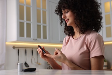 Photo of Diabetes. Woman using lancet pen at table in kitchen