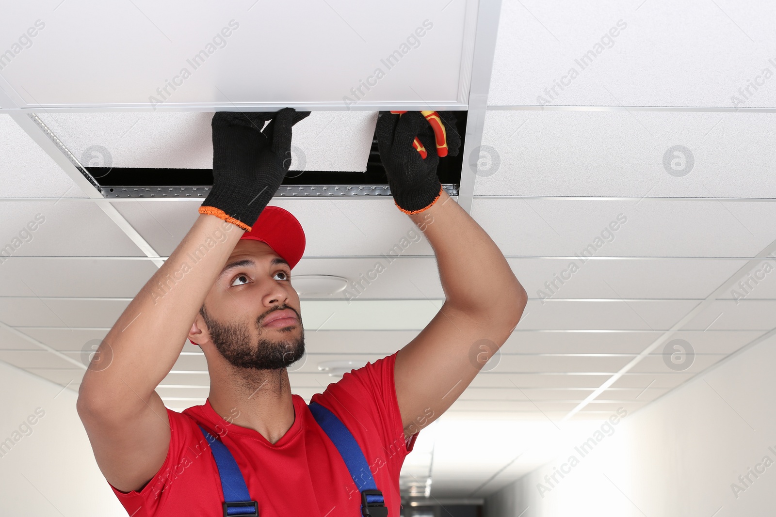 Photo of Electrician with pliers repairing ceiling light indoors, space for text