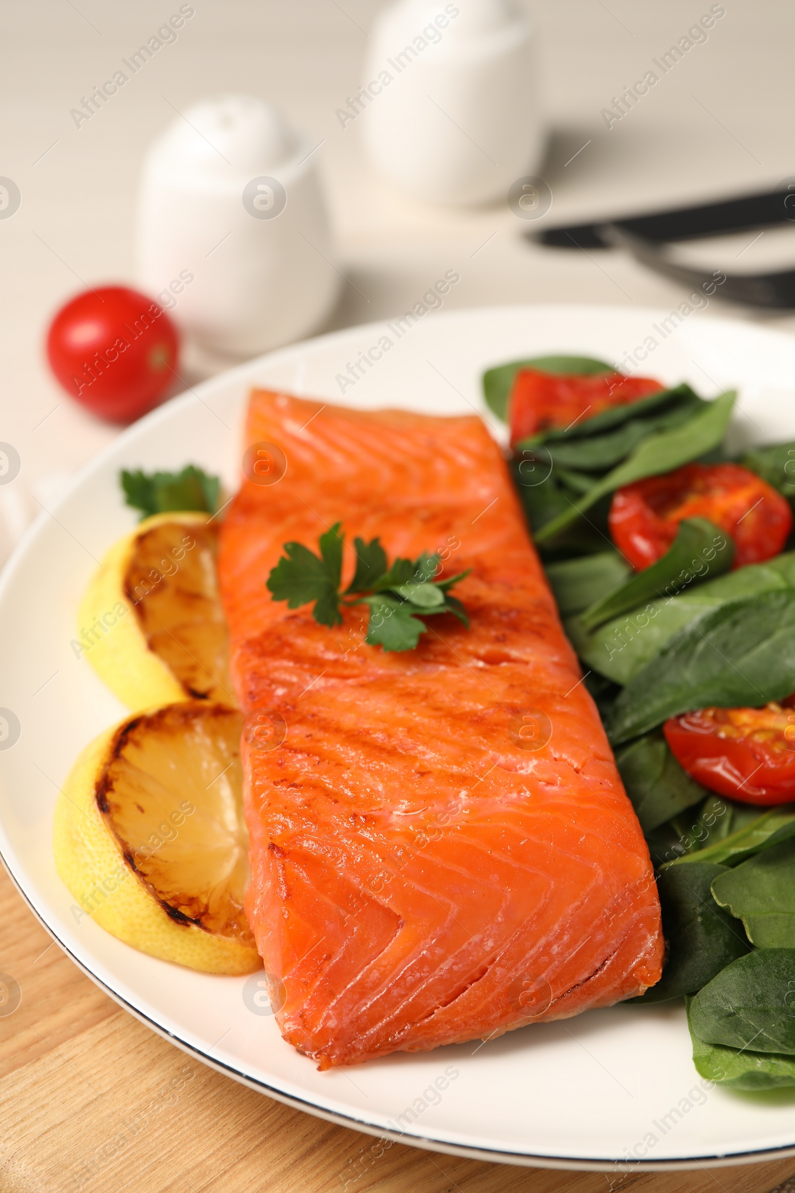 Photo of Tasty grilled salmon with basil, tomatoes and lemon on table, closeup