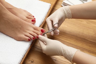 Photo of Pedicurist cutting client`s toenails with scissors in beauty salon, closeup