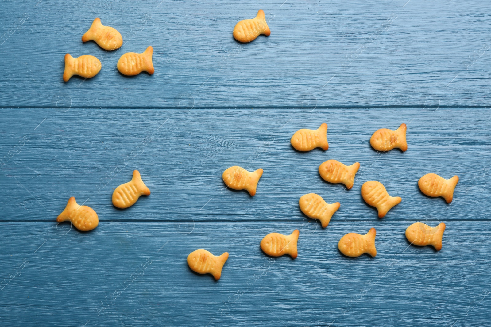 Photo of Delicious goldfish crackers on blue wooden table, flat lay